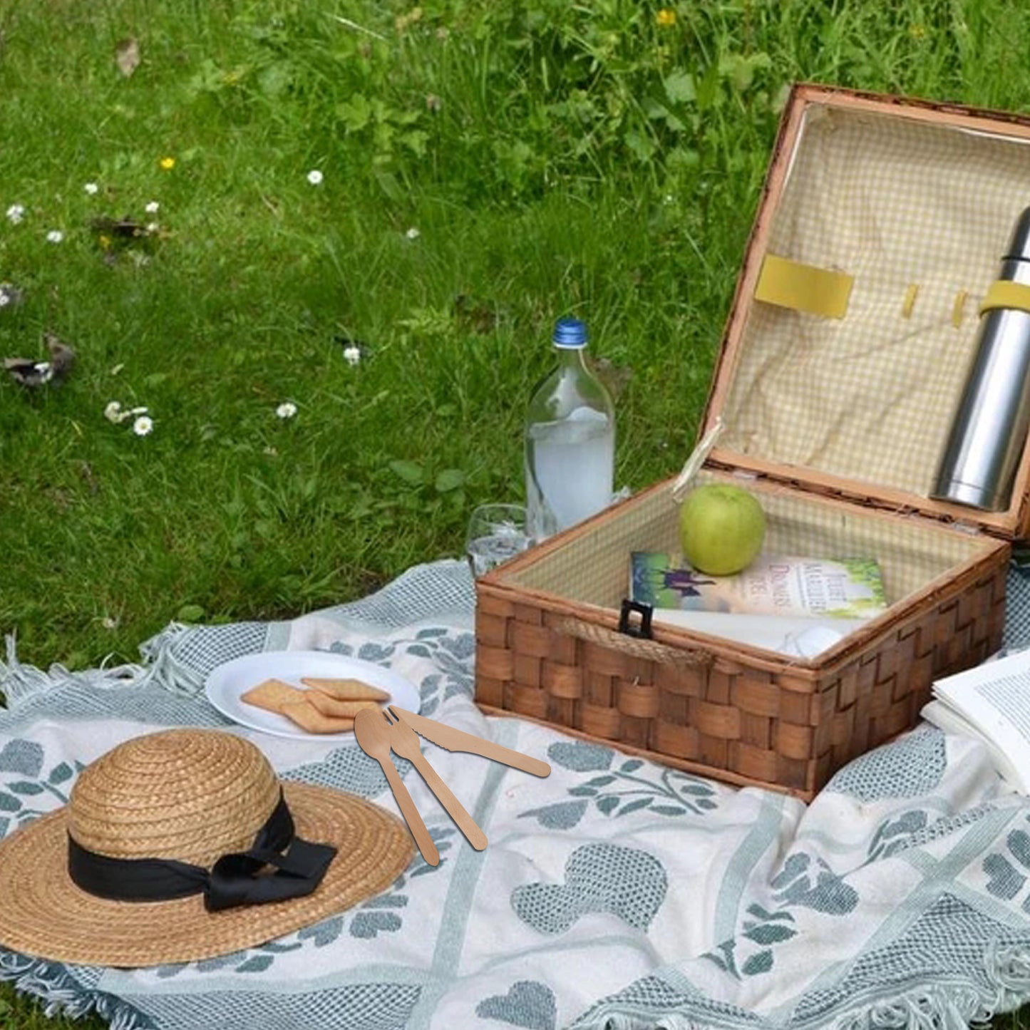 Woven picnic basket with straw hat cookies and thermos on checkered blanket