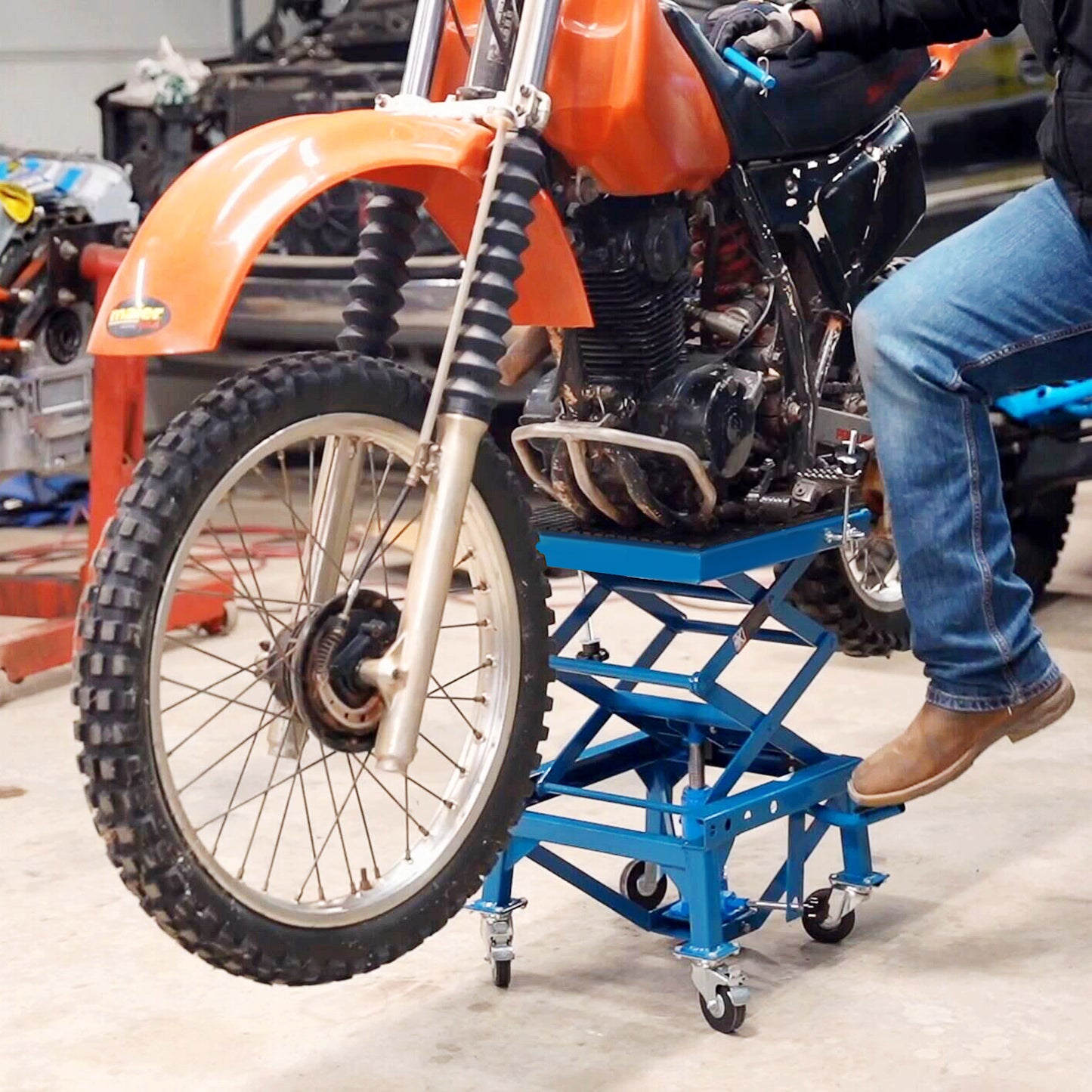 Orange dirt bike with knobby tires on a blue scissor lift in a workshop