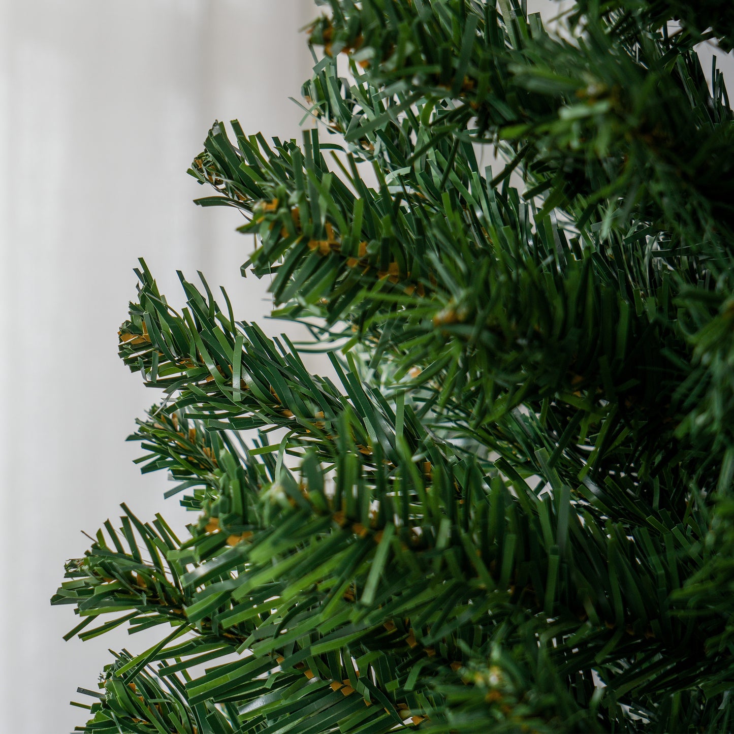 Closeup of realistic green artificial Christmas tree needles with golden accents ideal for holiday decor