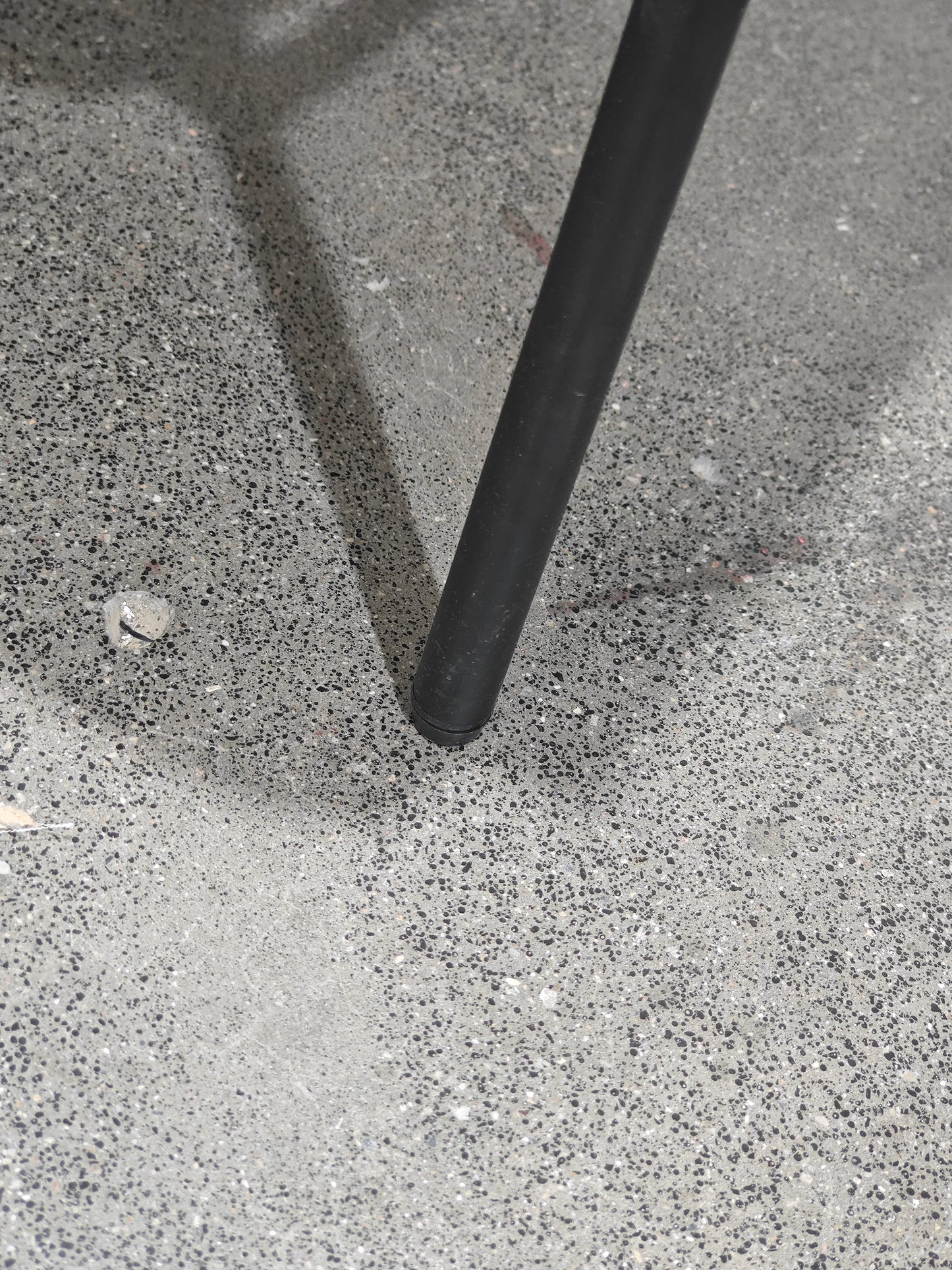 Black metal chair leg with rubber tip resting on textured concrete floor