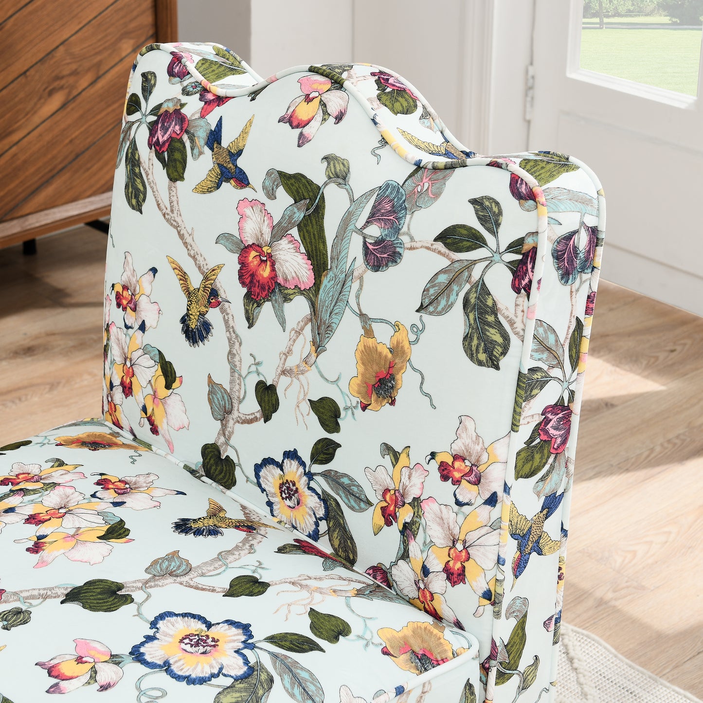 Closeup of a light blue armchair upholstered in a vibrant floral and bird pattern