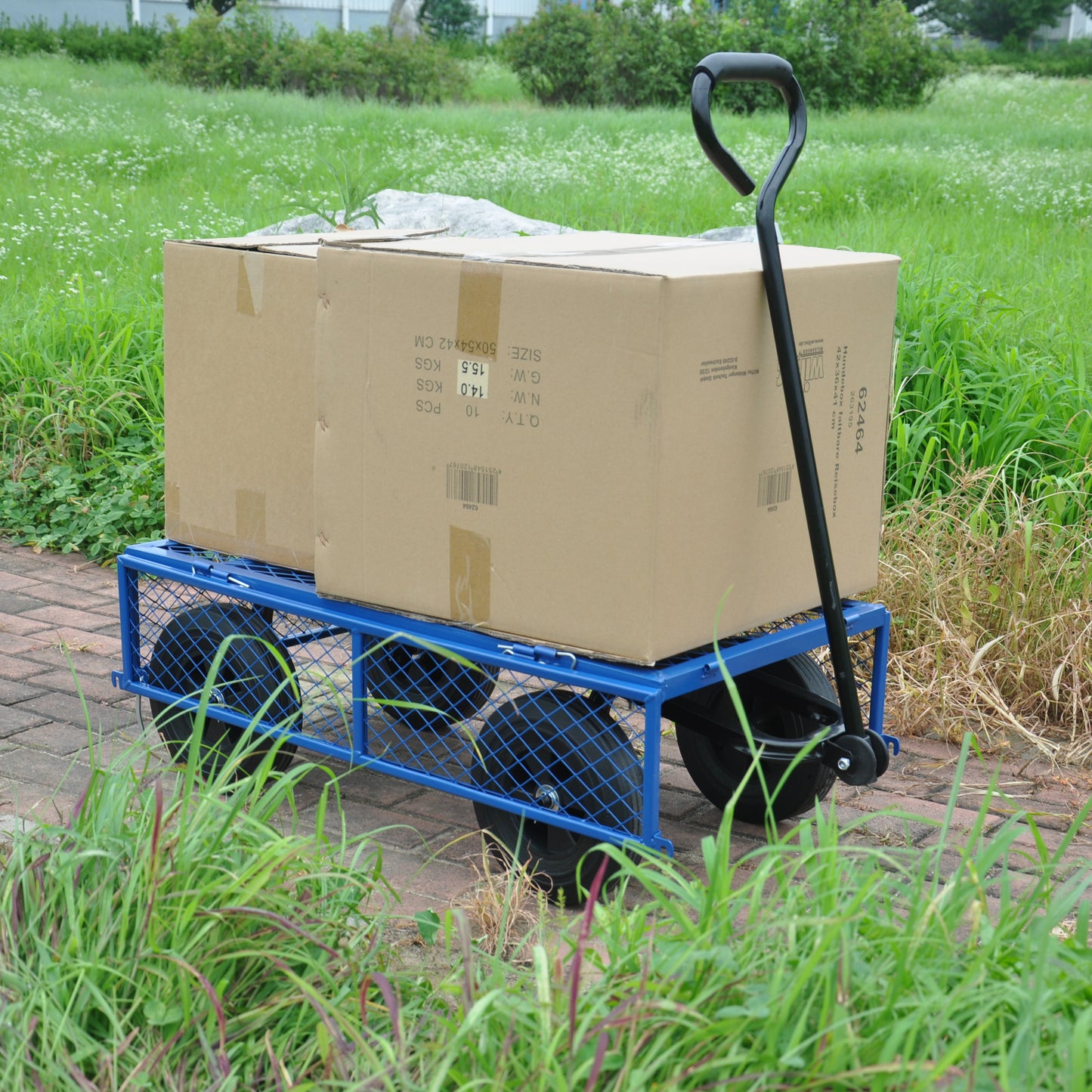 Blue garden utility cart loaded with two cardboard boxes on brick pathway