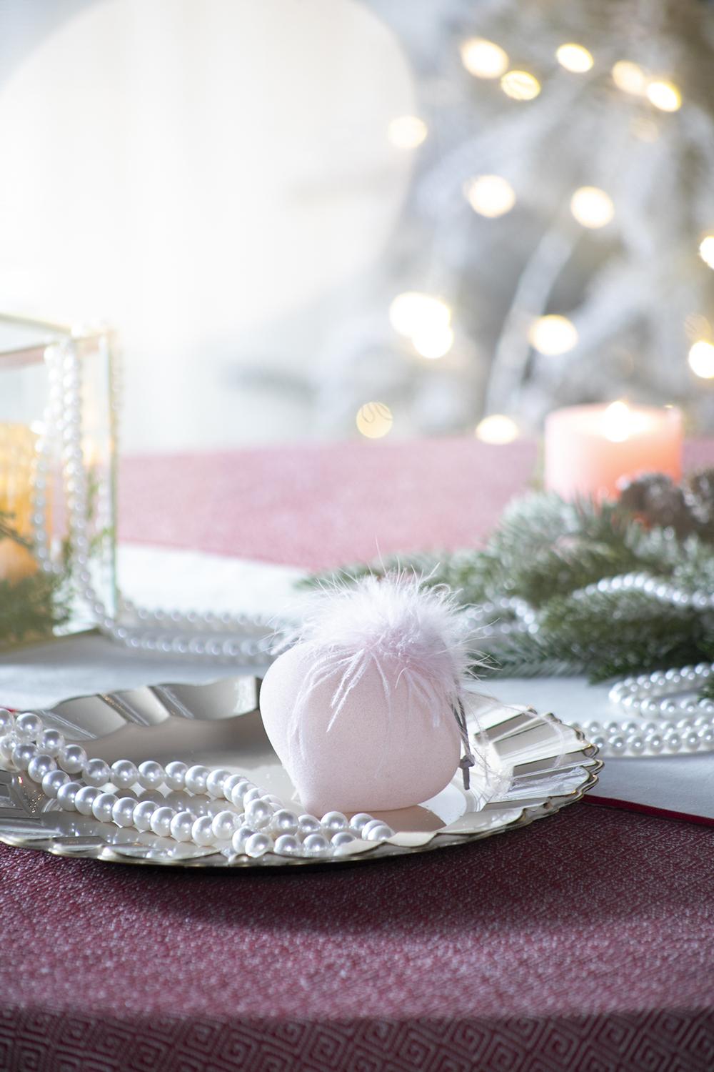 Delicate pink bath bomb with white feather topper on a silver tray with pearl necklaces