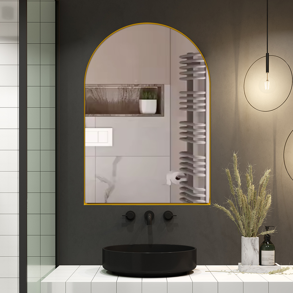 Arched gold framed bathroom mirror reflecting a modern vanity with plants