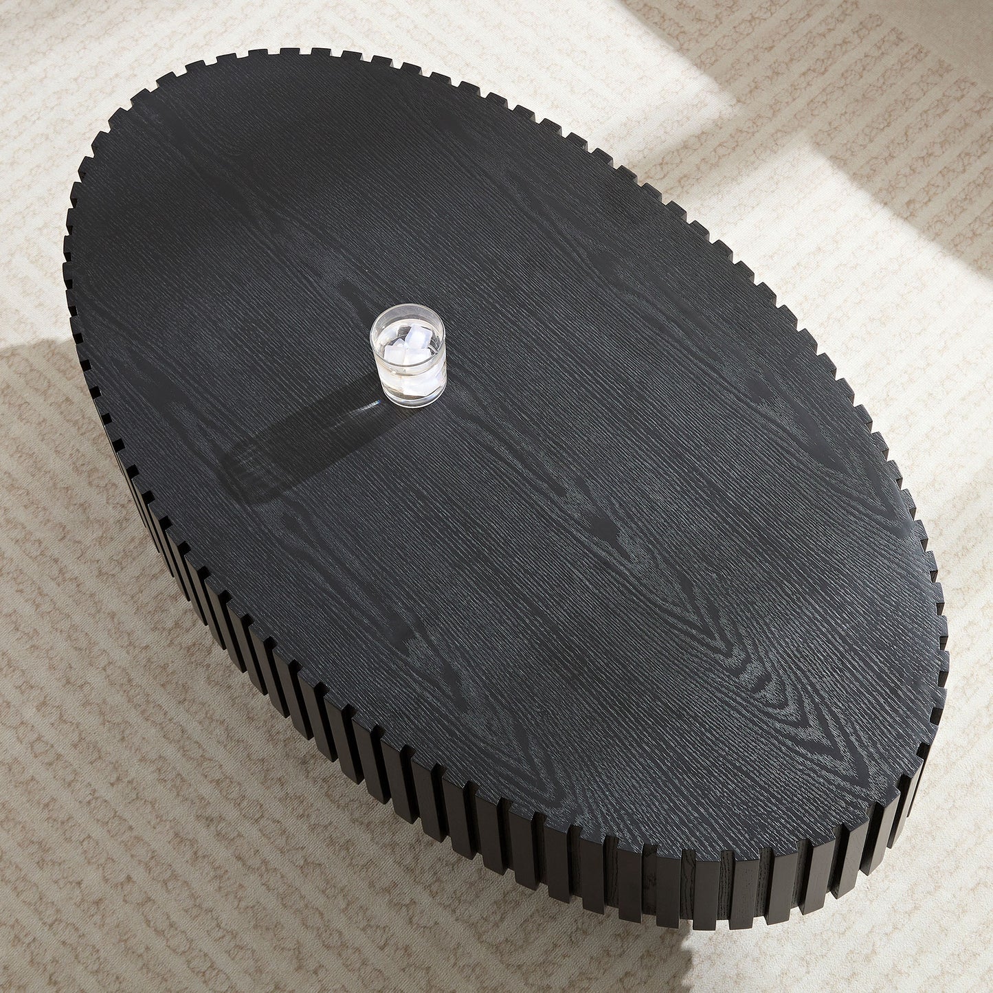 Black oval coffee table with ribbed wood texture and a glass of water
