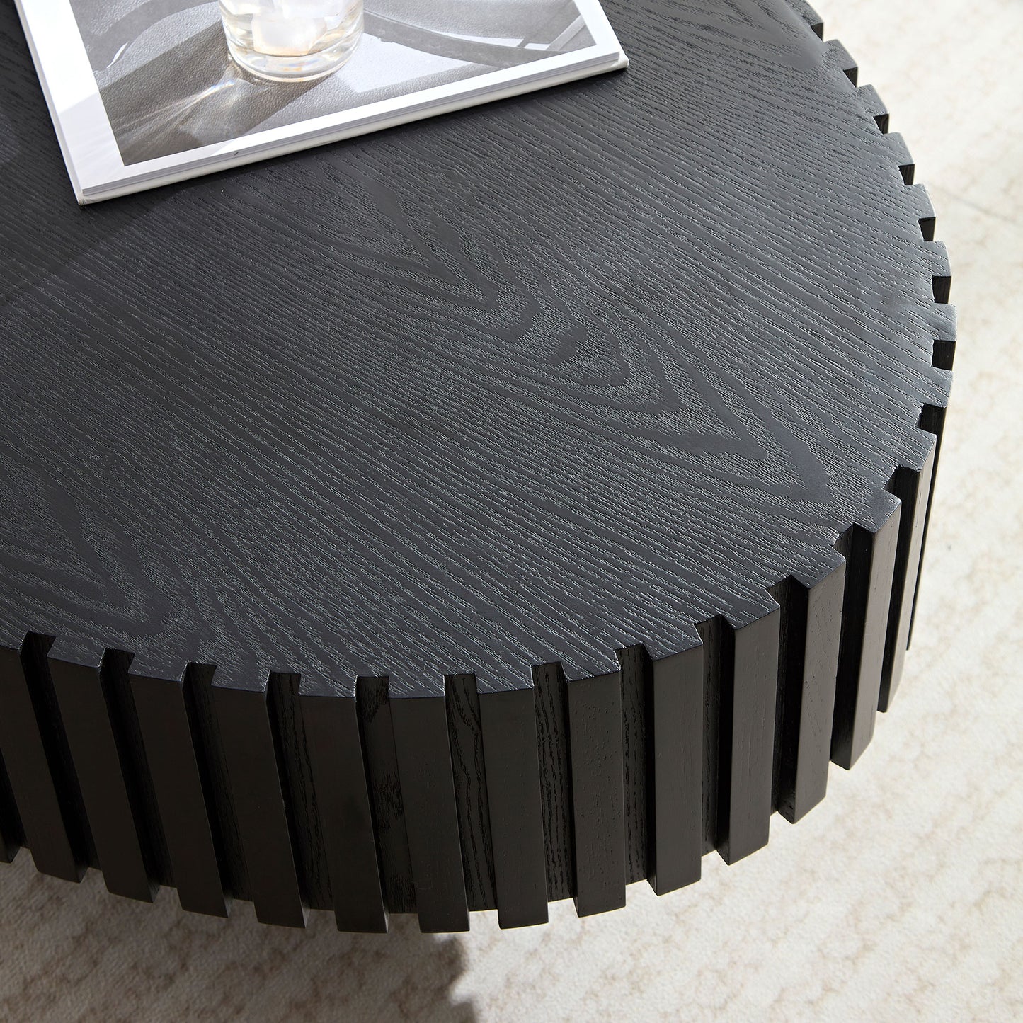 Black round coffee table with carved wooden details on the side featuring a magazine and drink