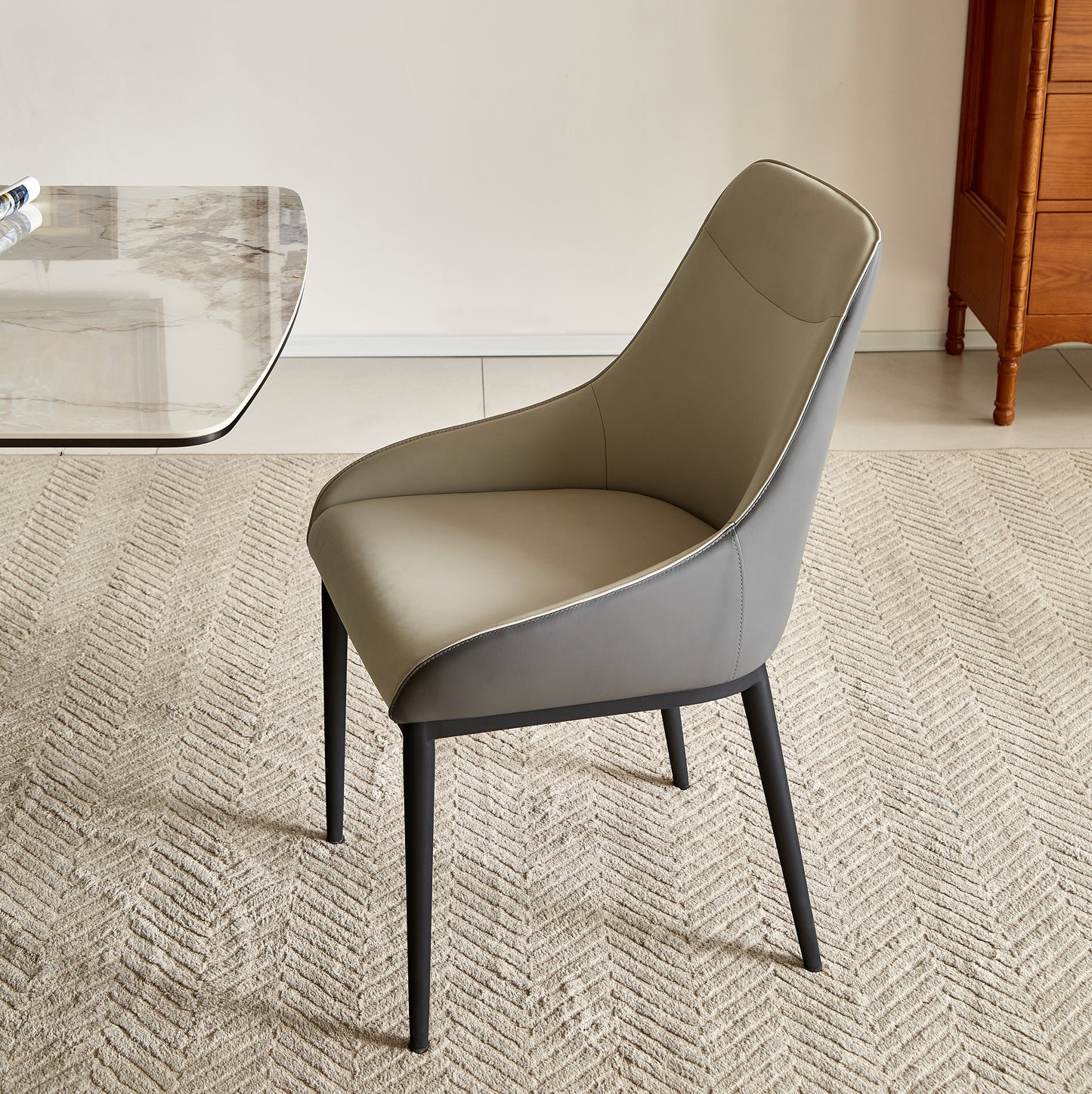 Modern gray leather dining chair with black metal legs on a textured rug