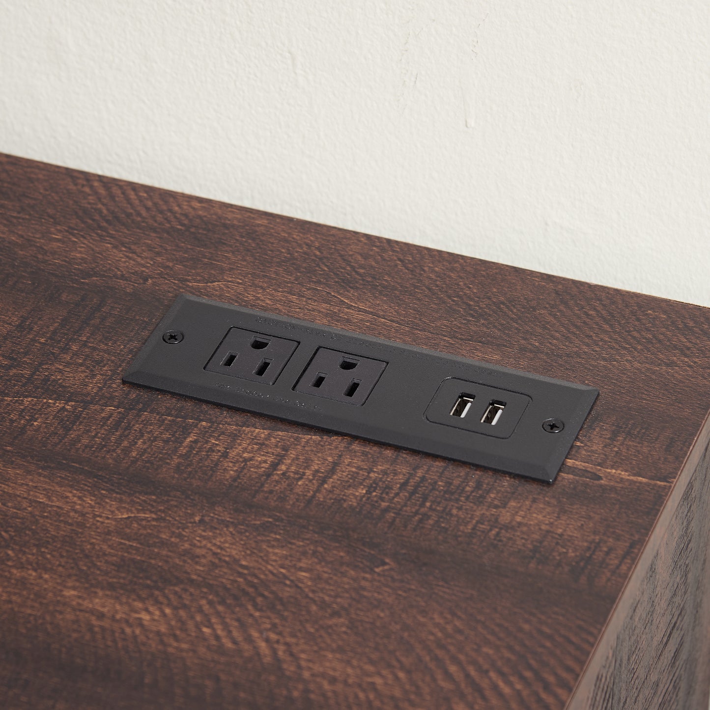 Flush mount power outlet with two AC sockets and two USB ports on a dark wood surface