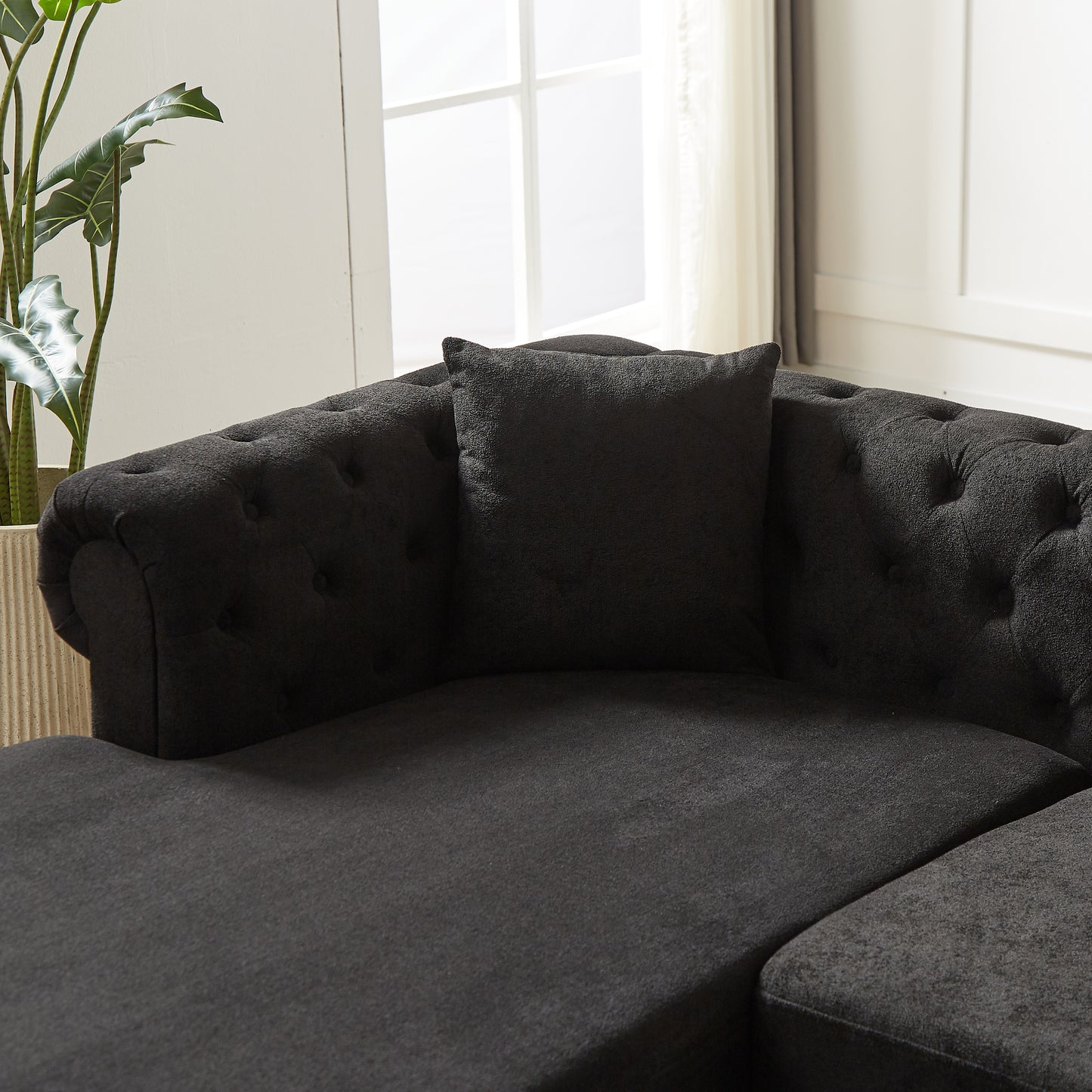 Dark grey tufted fabric sectional sofa with a plush accent pillow