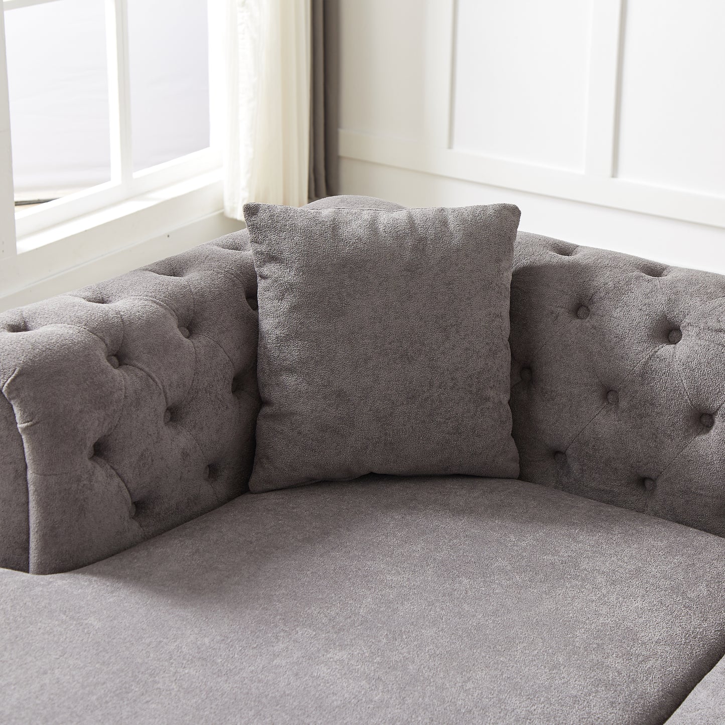 Closeup of a gray chenille tufted sofa with a matching throw pillow