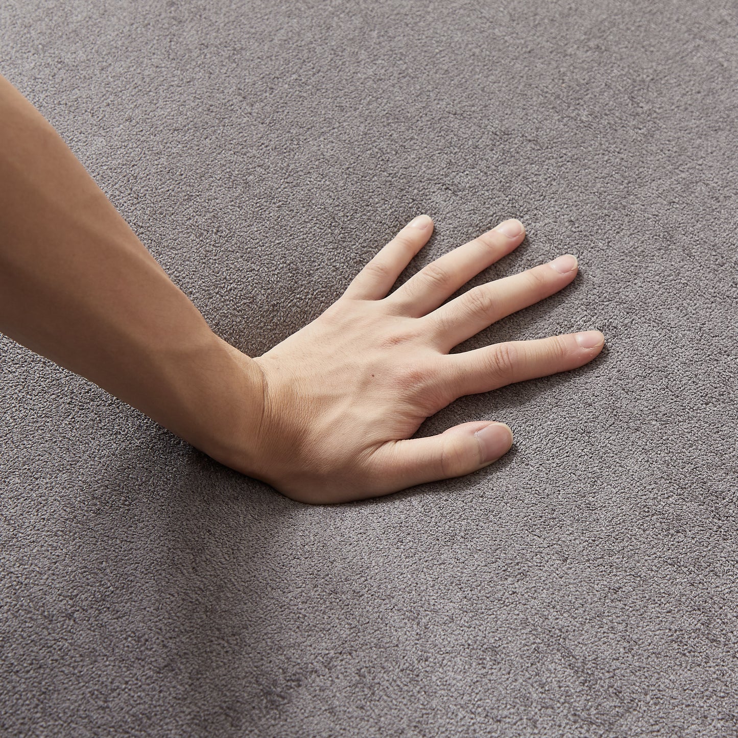 A hand presses into plush grey carpet showing its soft texture