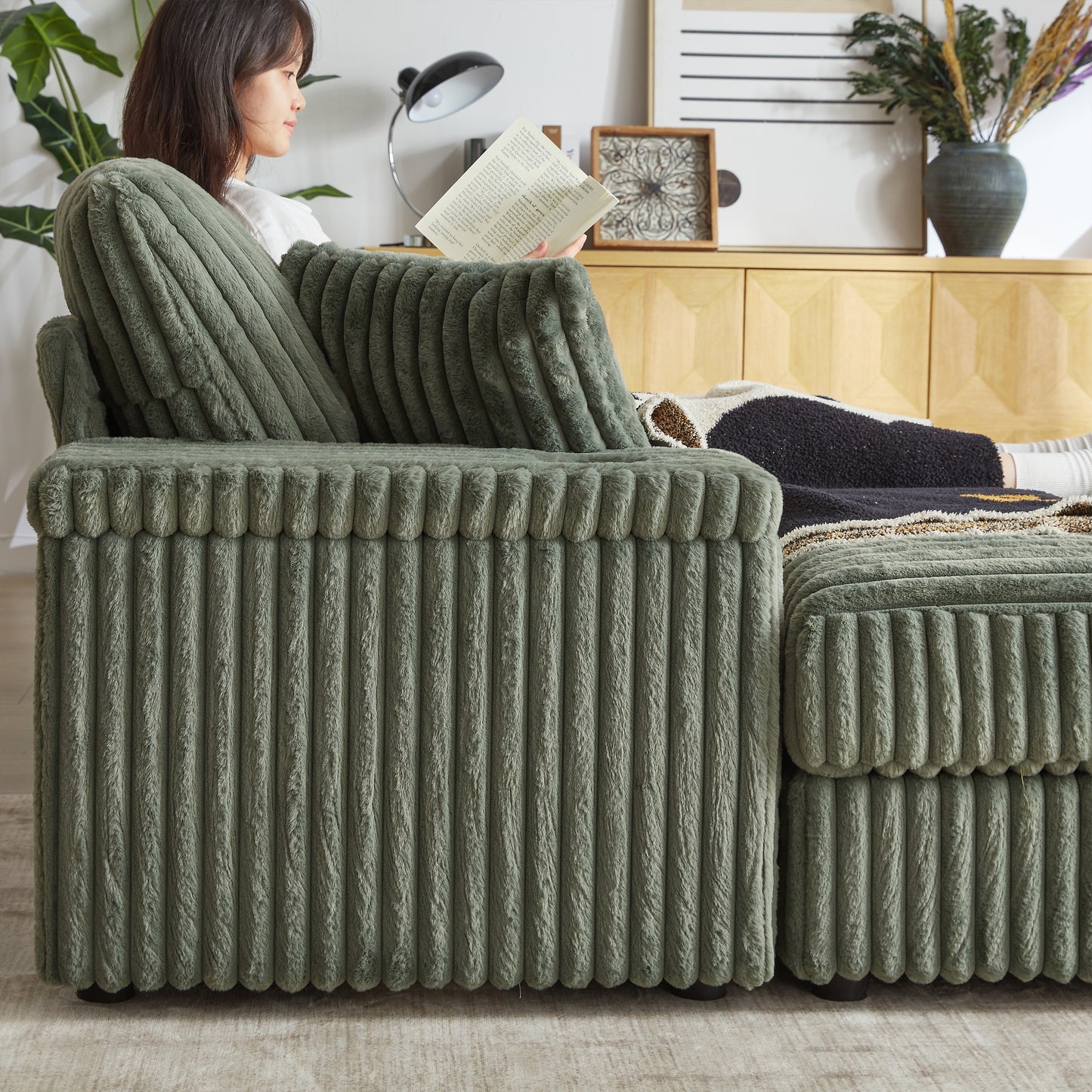 Sage green plush corduroy sectional sofa with a relaxed woman reading a book on it