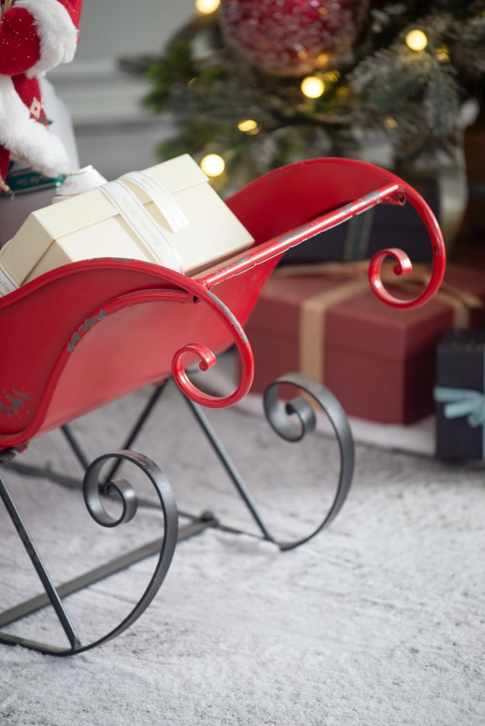 Antique red metal sleigh decoration holding a cream gift box with white ribbon
