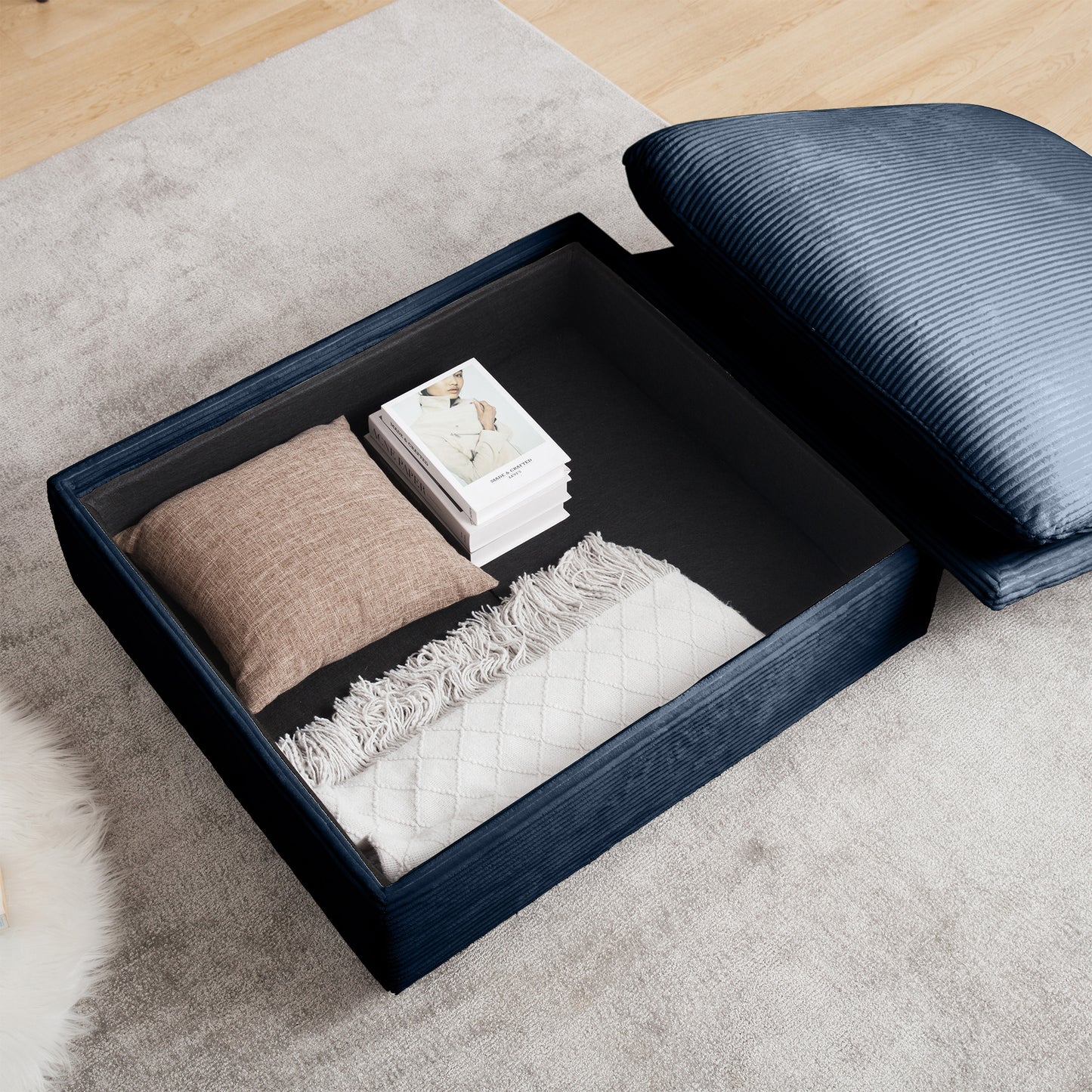 Navy blue upholstered ottoman with open storage revealing books and throws