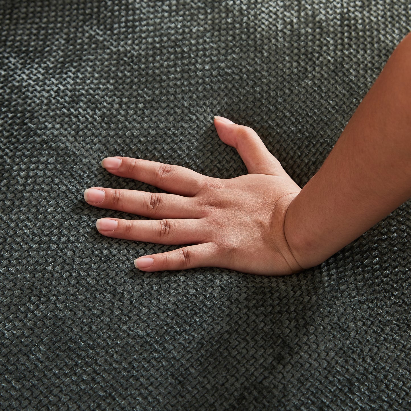 Hand touching dark grey textured chenille fabric for sofa upholstery showcasing its soft feel