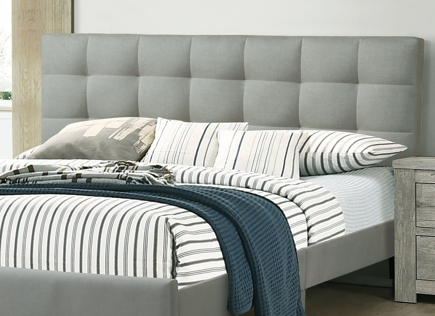Grey upholstered bed frame with tufted headboard and striped bedding