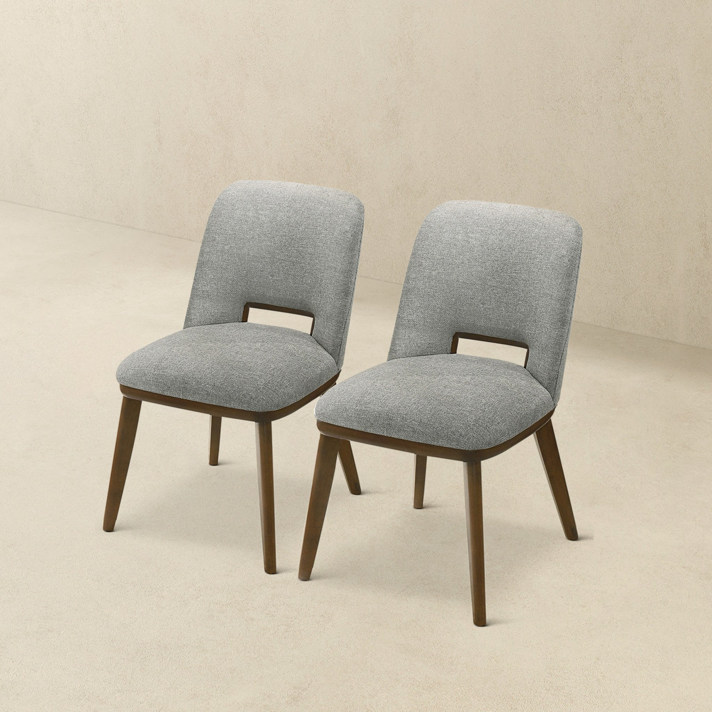 Two grey upholstered dining chairs with dark wood legs and cutout back detail