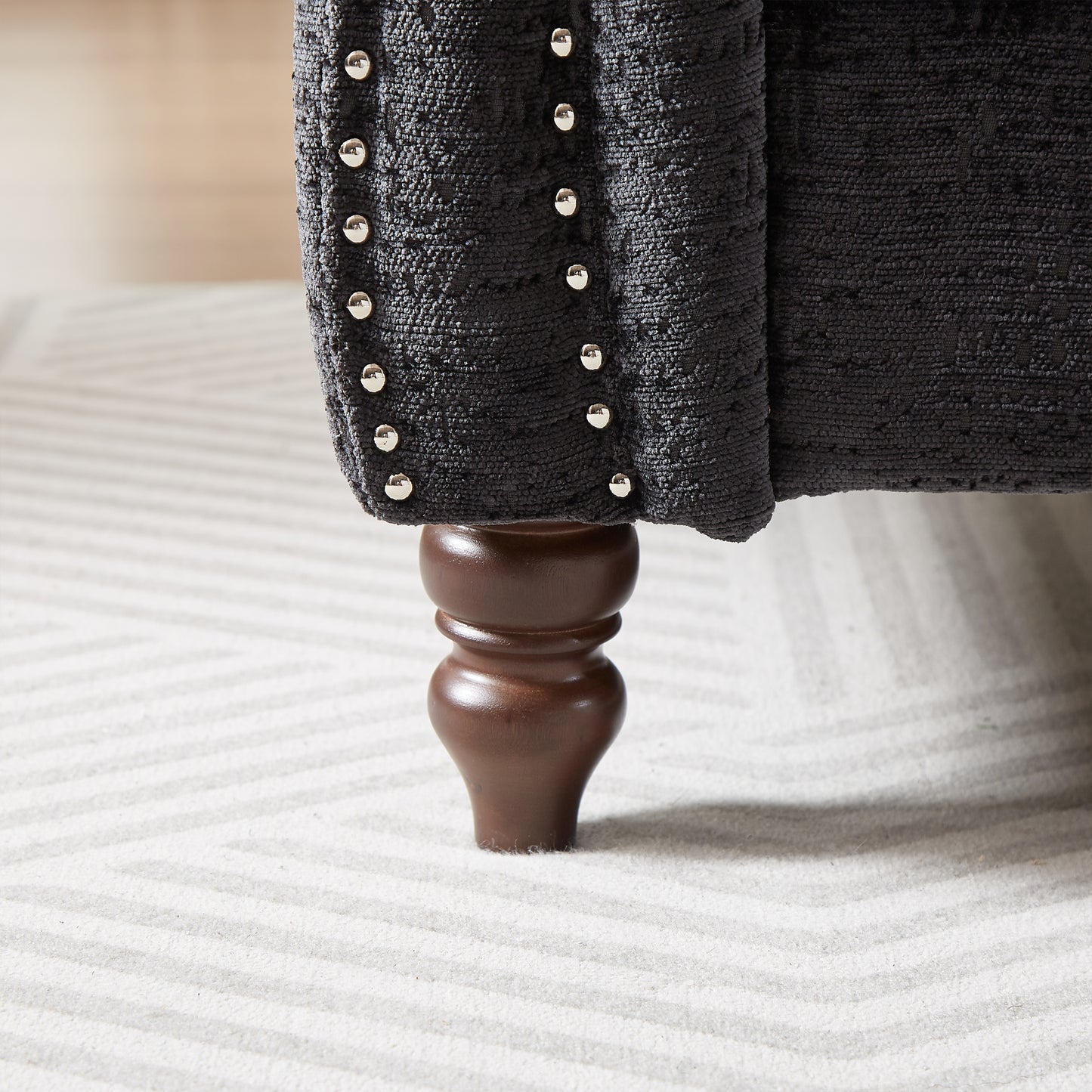 Dark grey textured upholstery armchair with silver nailhead trim and a carved wood leg