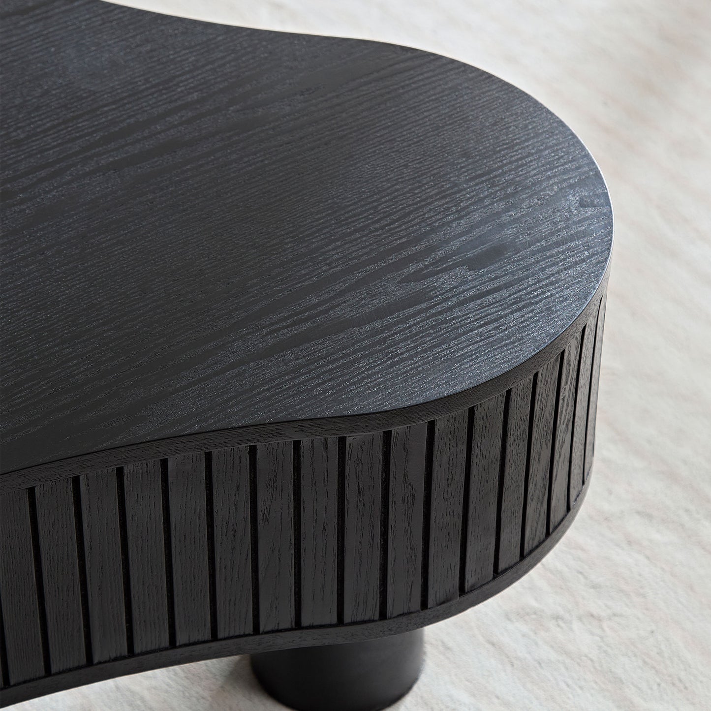 Closeup of a black wood coffee table with a textured surface and fluted sides