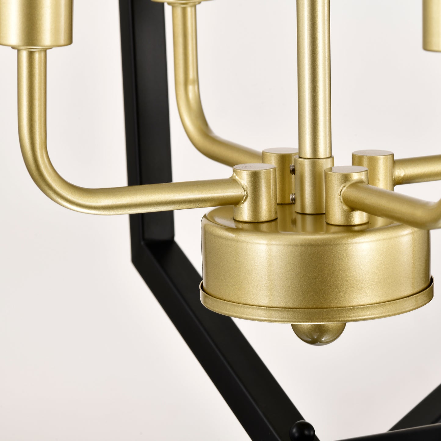 Closeup of a brushed brass chandelier arm connecting to a black metal frame