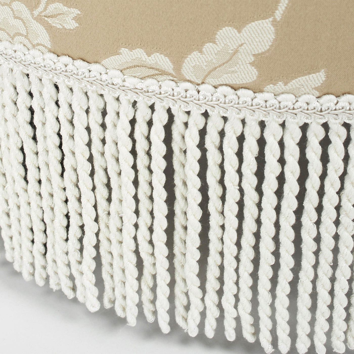 Beige upholstered ottoman with detailed white rope fringe