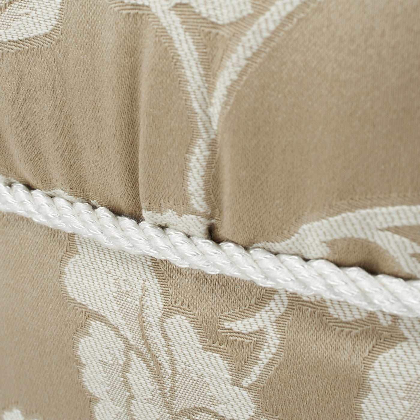 Beige upholstered cushion with rope trim and floral pattern detail