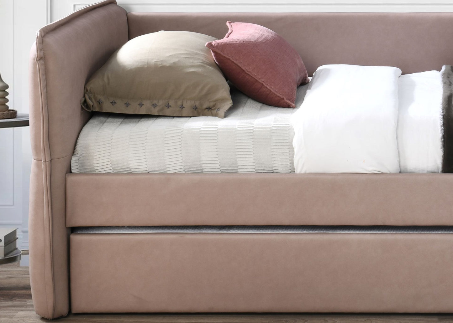 Dusty rose upholstered daybed with tufted pink and beige pillows on a white striped comforter