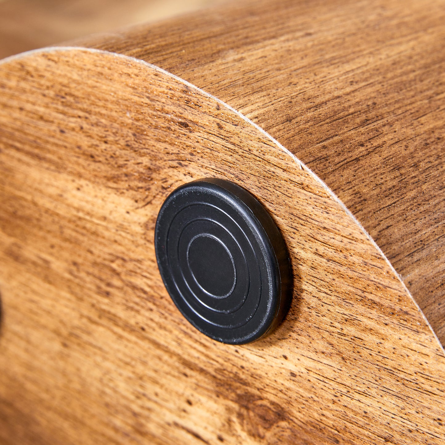 Closeup of a black circular drawer knob on a woodgrain finished cabinet door