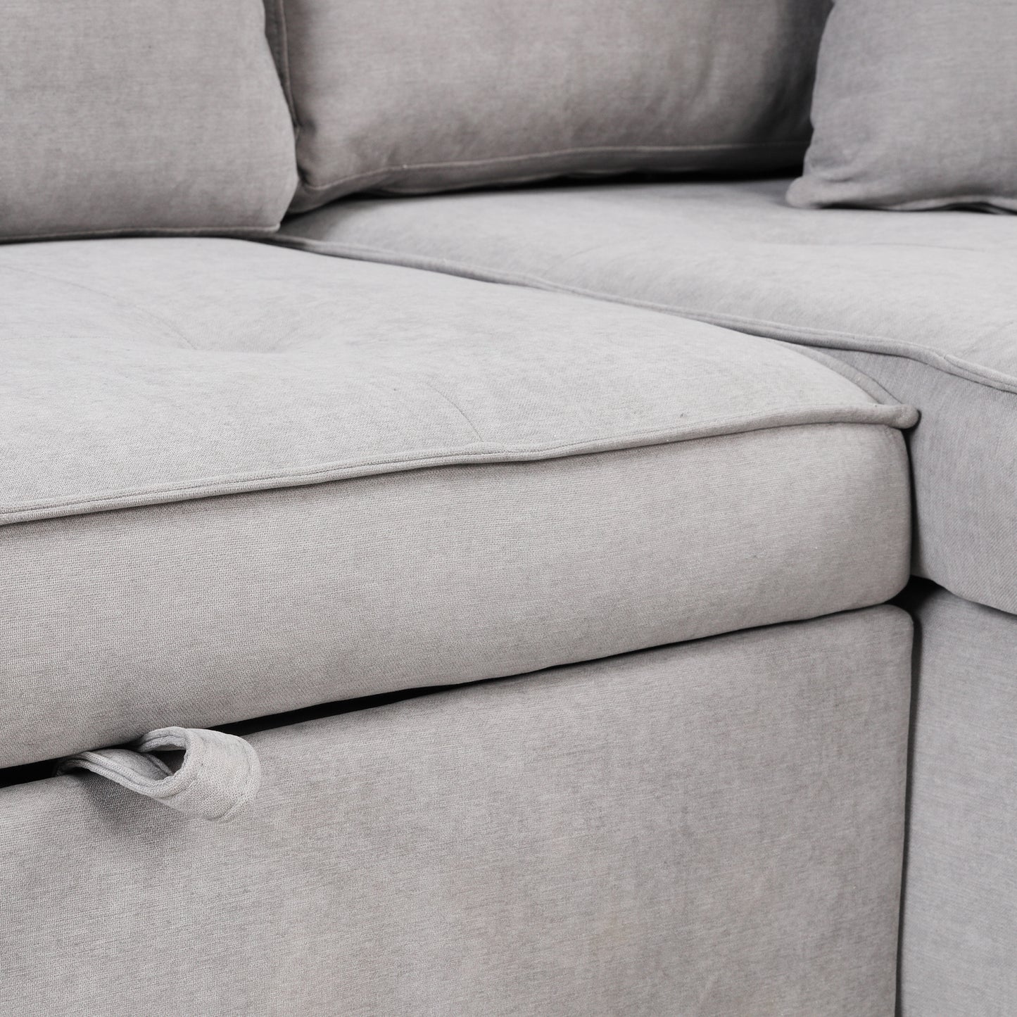 Closeup of a light grey linen fabric sectional sofa with tufted cushions and piping