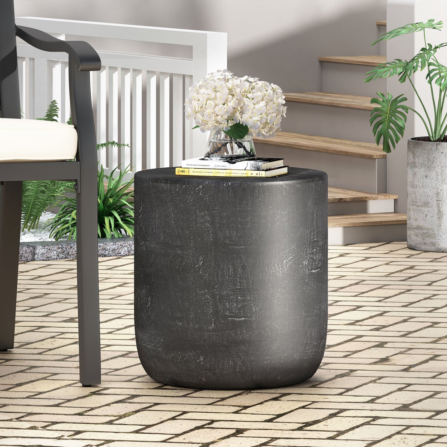 Dark grey round patio side table with textured finish books and flowers on top