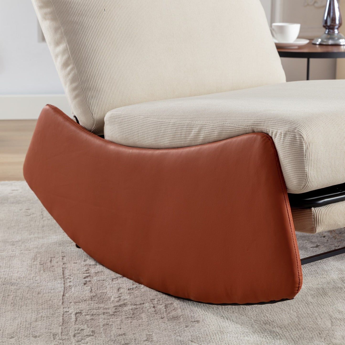 Closeup of a modern rocking chair with cream corduroy upholstery and a curved cognac leather base