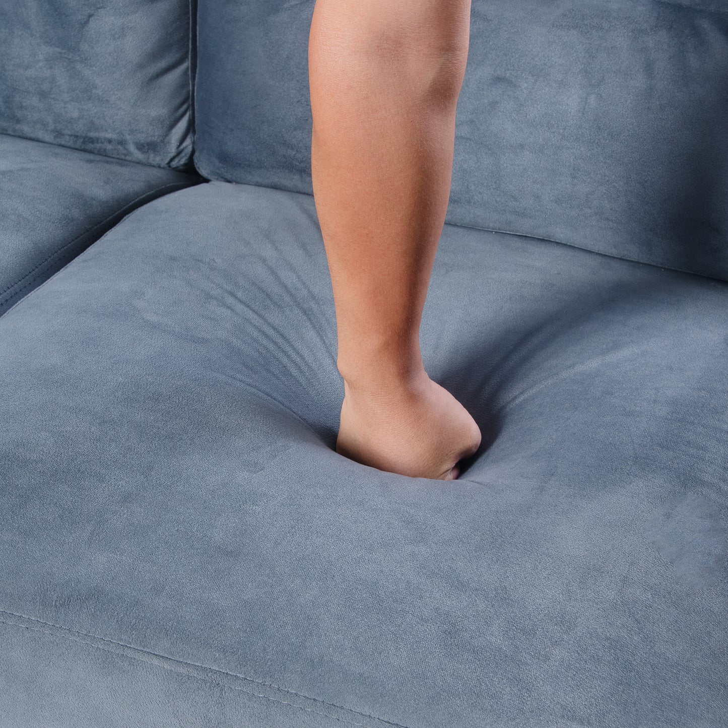 Hand pressing into plush grey sofa cushion demonstrating softness