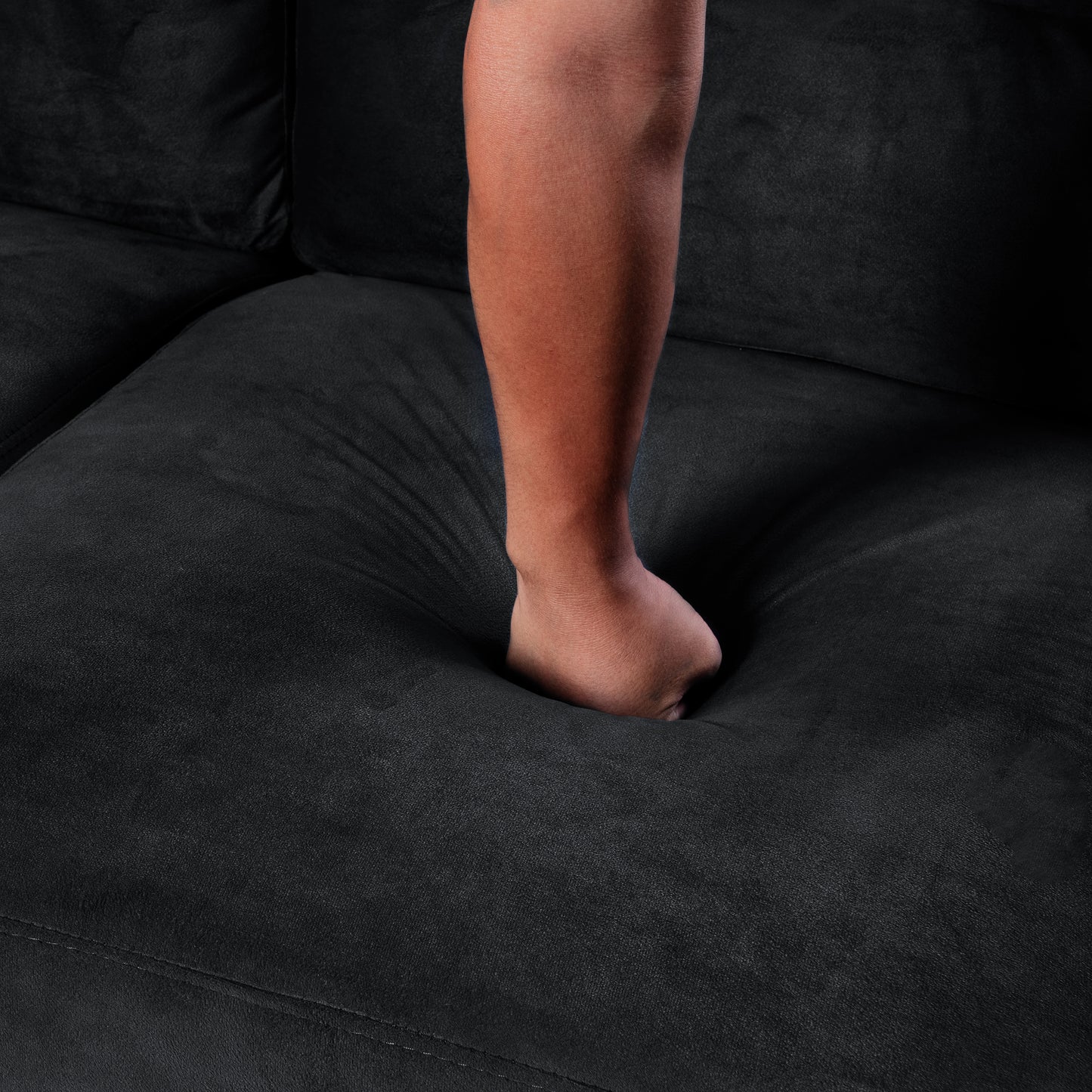 Black microfiber couch cushion sinks deeply under hand pressure showing plush comfort