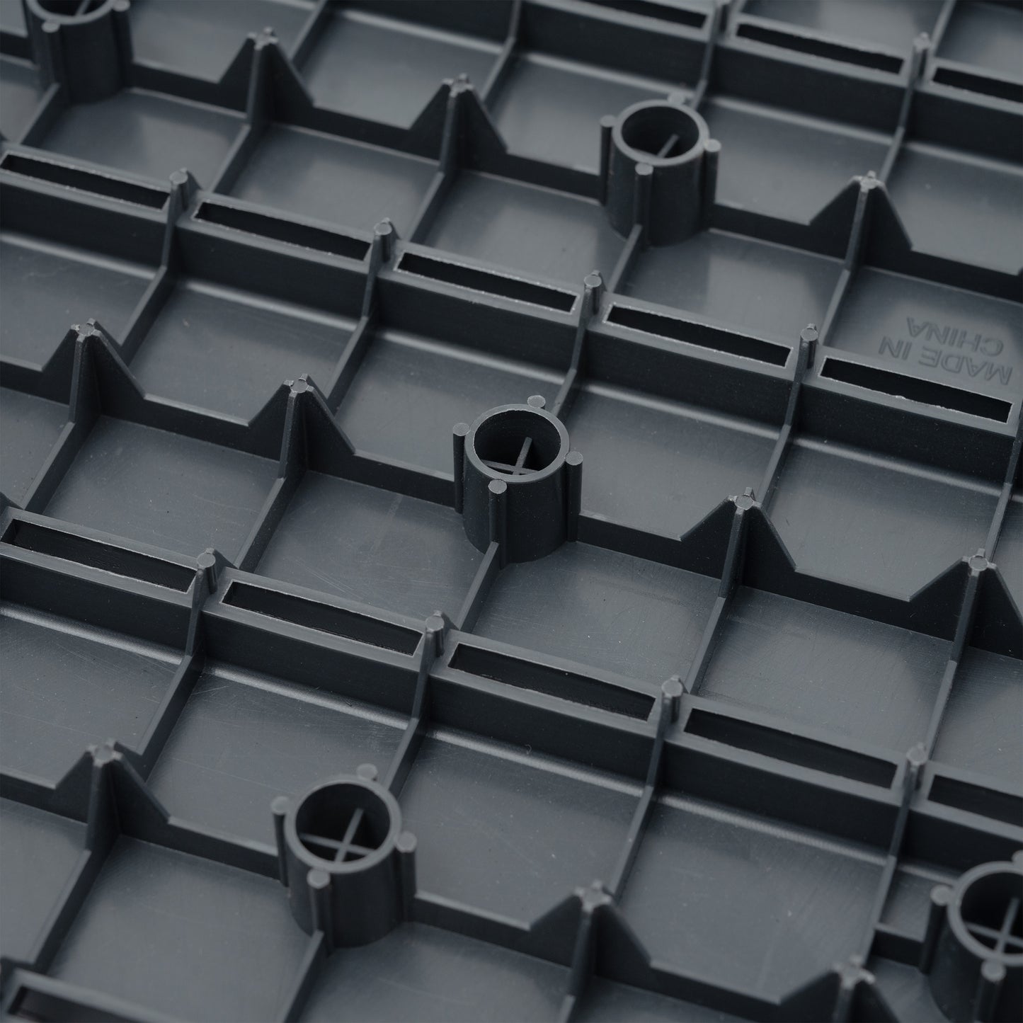 Dark gray interlocking floor tile base with raised grid pattern and circular supports