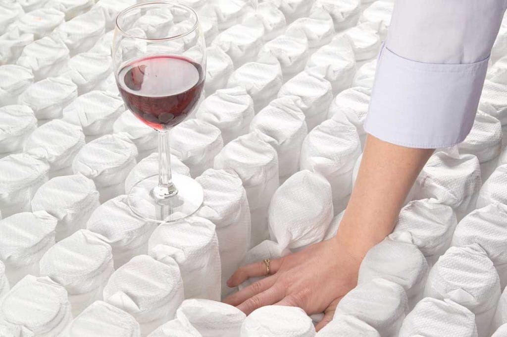 Pocket springs in a white fabric demonstrating mattress support with a wine glass