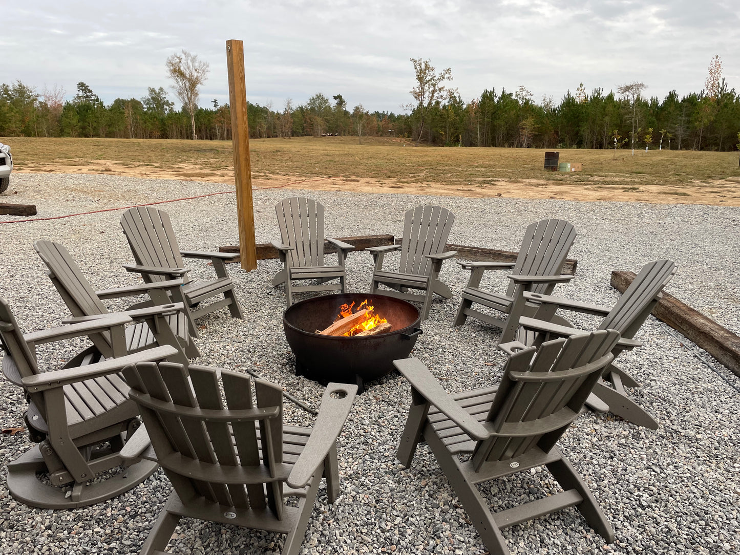 Round metal fire pit with glowing embers surrounded by gray Adirondack chairs on gravel