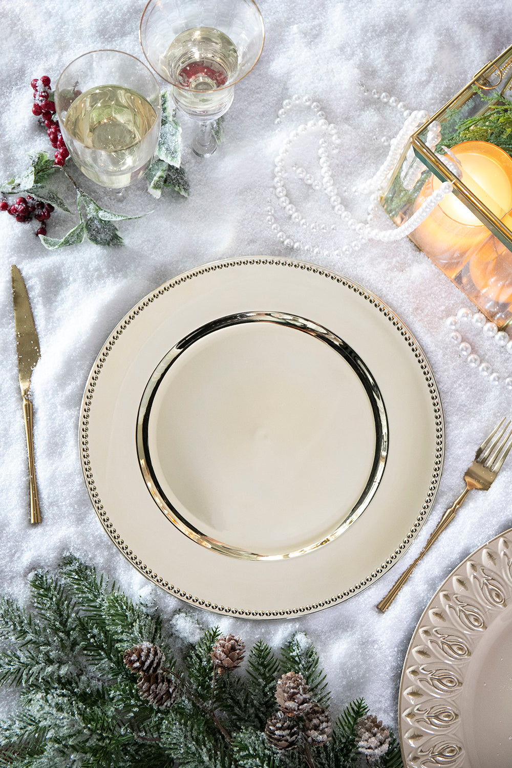 Cream charger plate with gold rim and beaded edge set on a snowy table