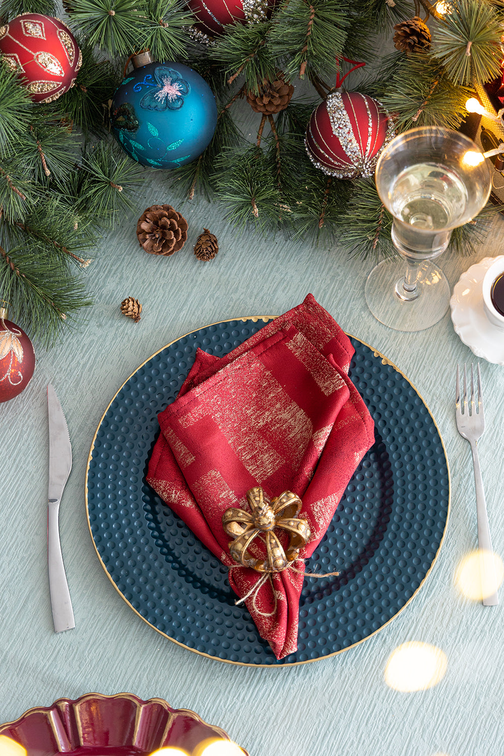 Festive red napkin with gold accents and crown napkin ring on dark blue charger plate