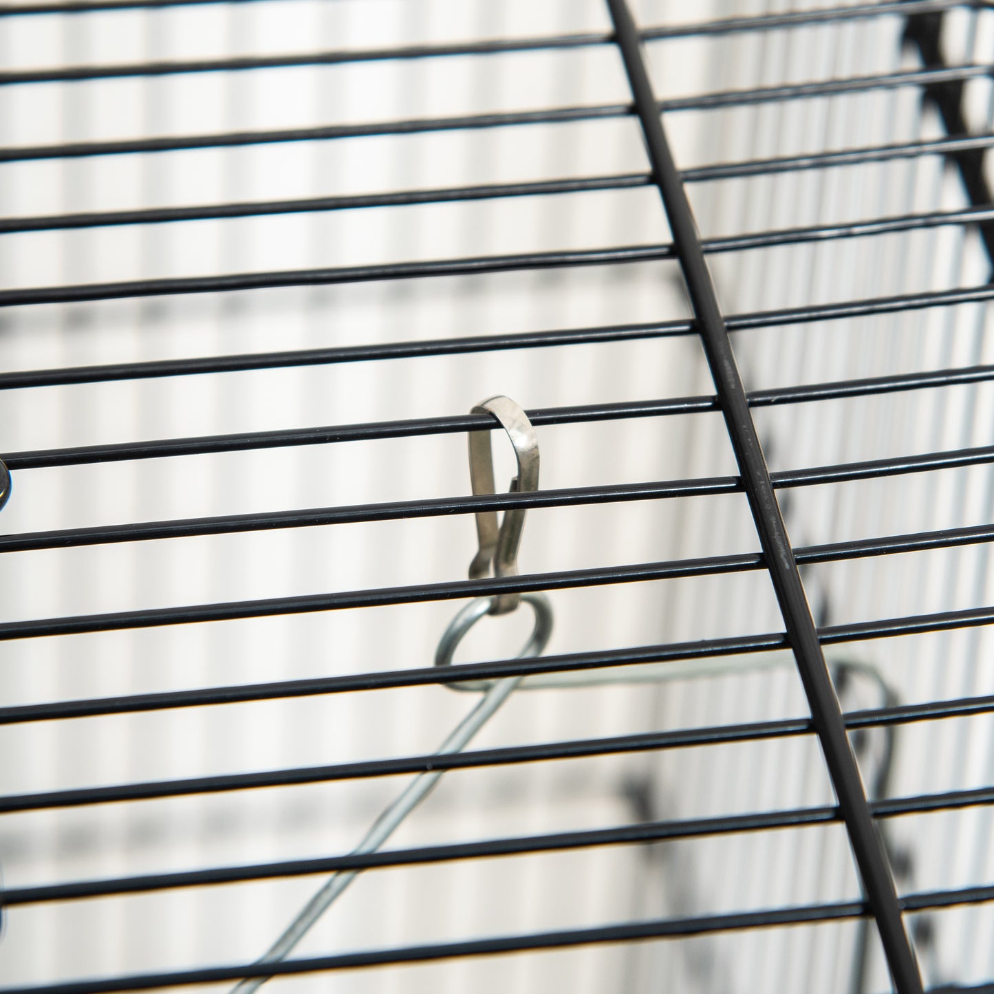 Closeup of a black metal cage grate with a silver clip attached to a wire hanger