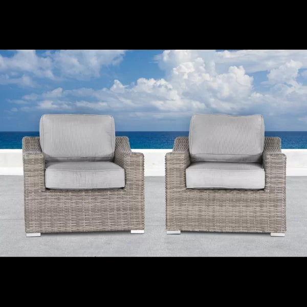 Two grey wicker patio chairs with plush cushions on a concrete patio with ocean backdrop