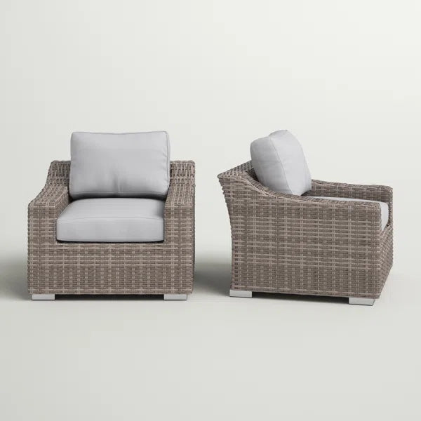 Two taupe wicker outdoor accent chairs with plush grey cushions sit on a white background