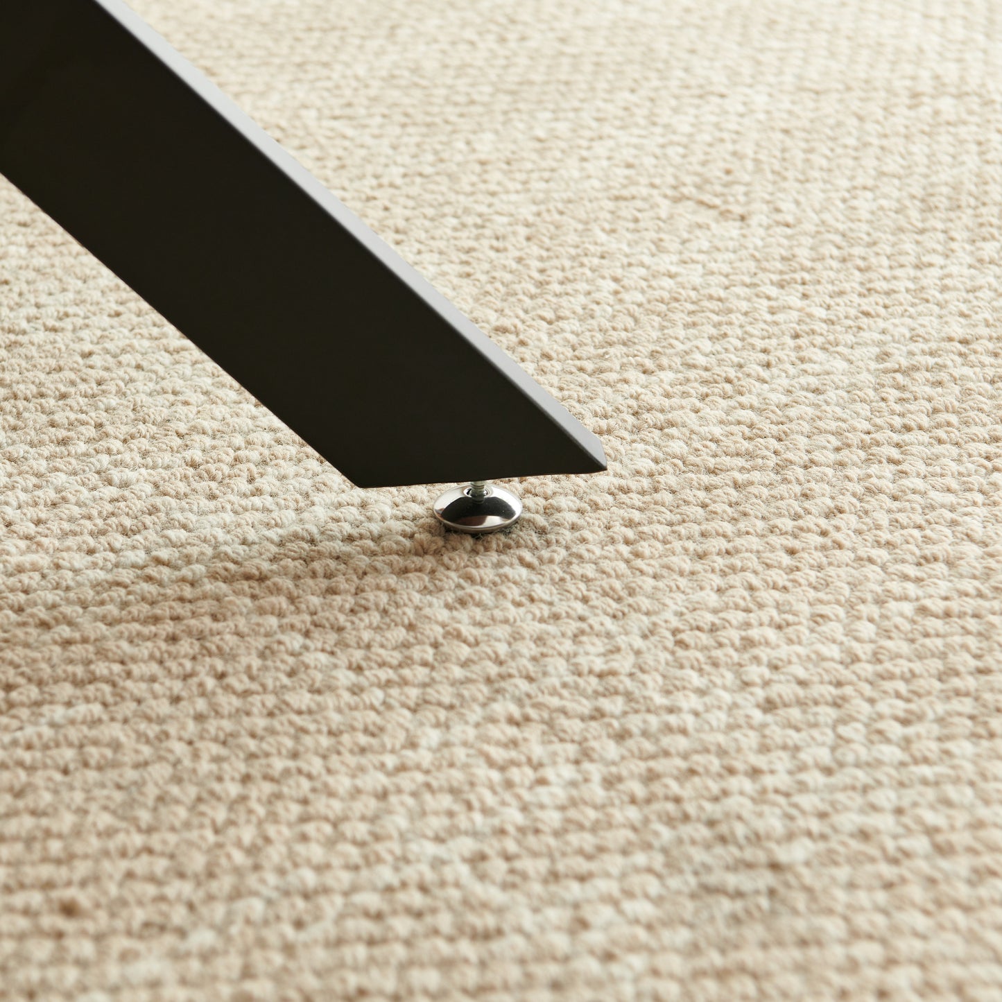 Black metal table leg with chrome foot rests on textured beige carpet