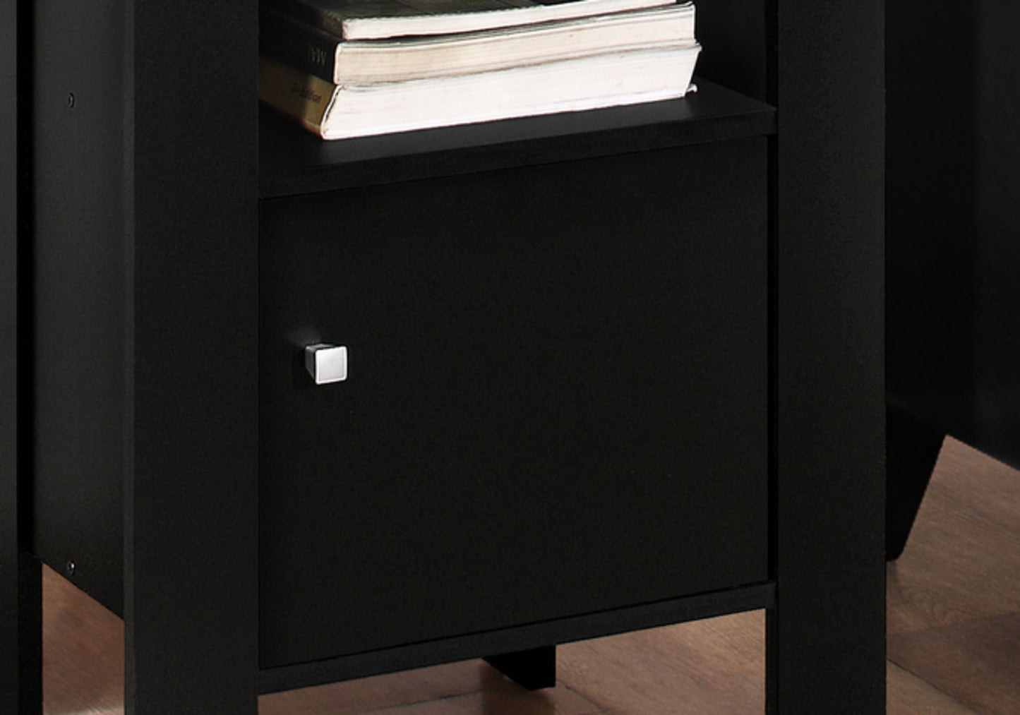Closeup of a black nightstand with a silver square knob on its cabinet door