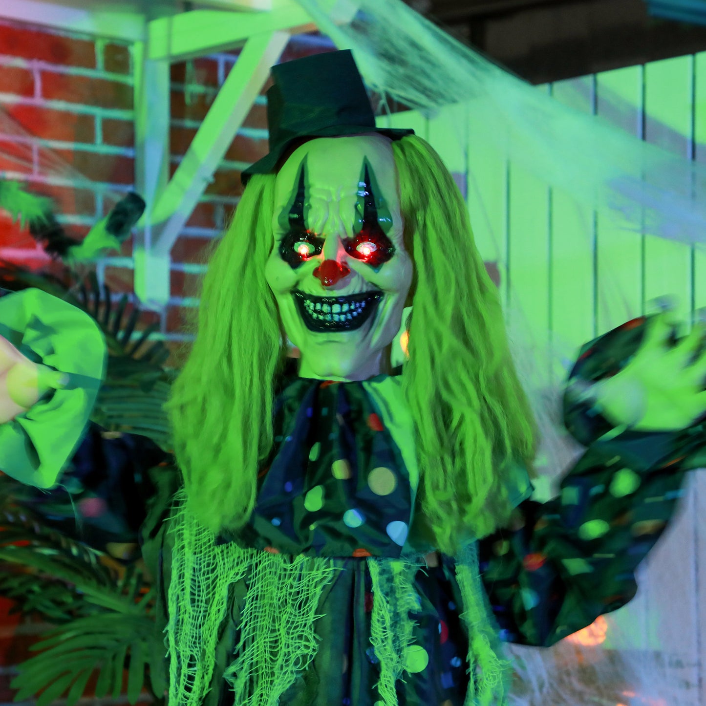 Scary green clown prop with glowing red eyes and a black top hat