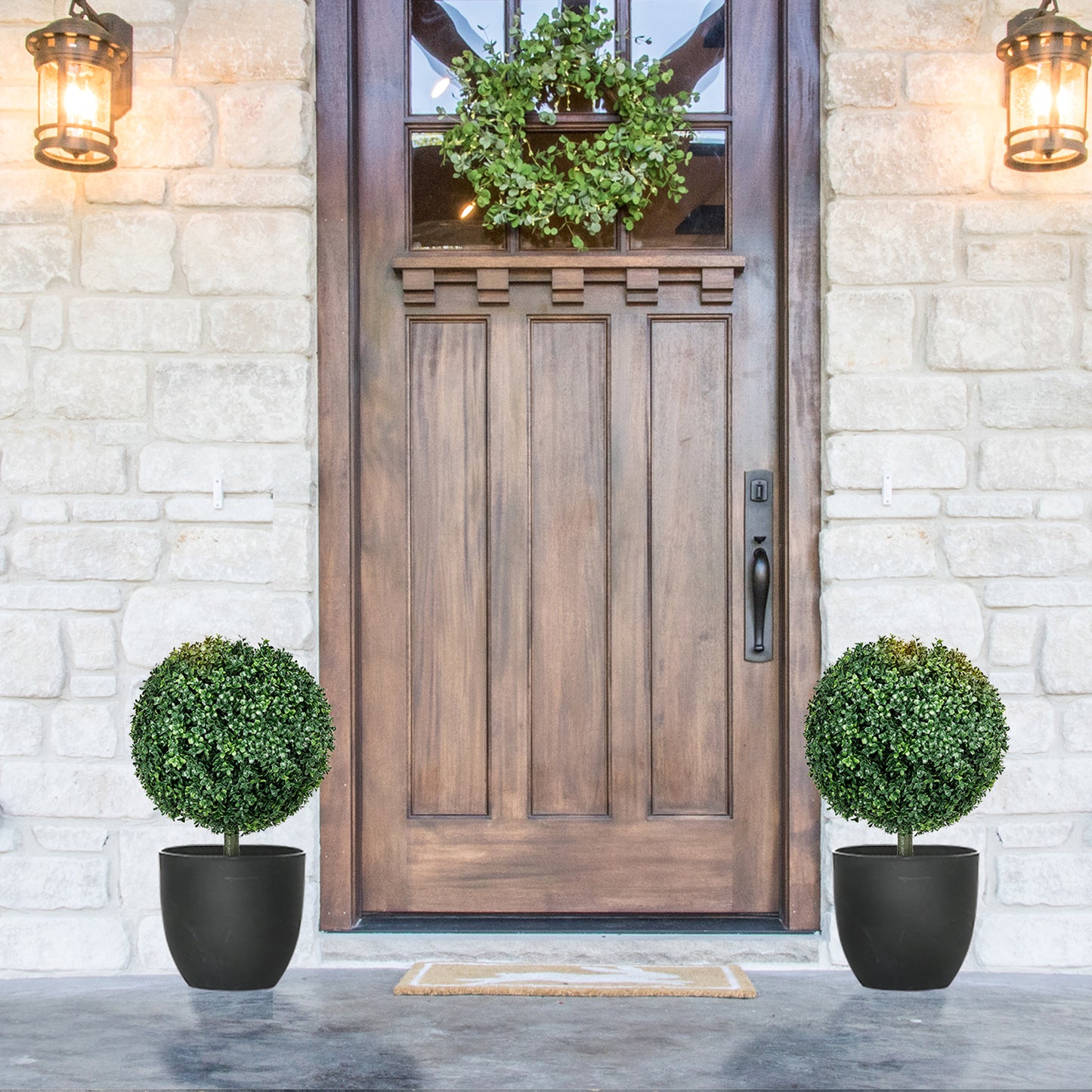 Pair of artificial boxwood topiary balls in black pots flanking a wooden door