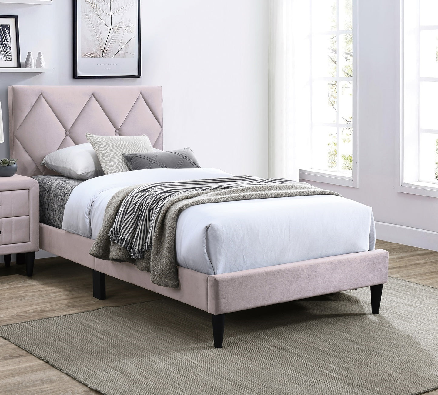 Pink velvet diamondtufted twin bed with dark tapered legs and grey striped throw