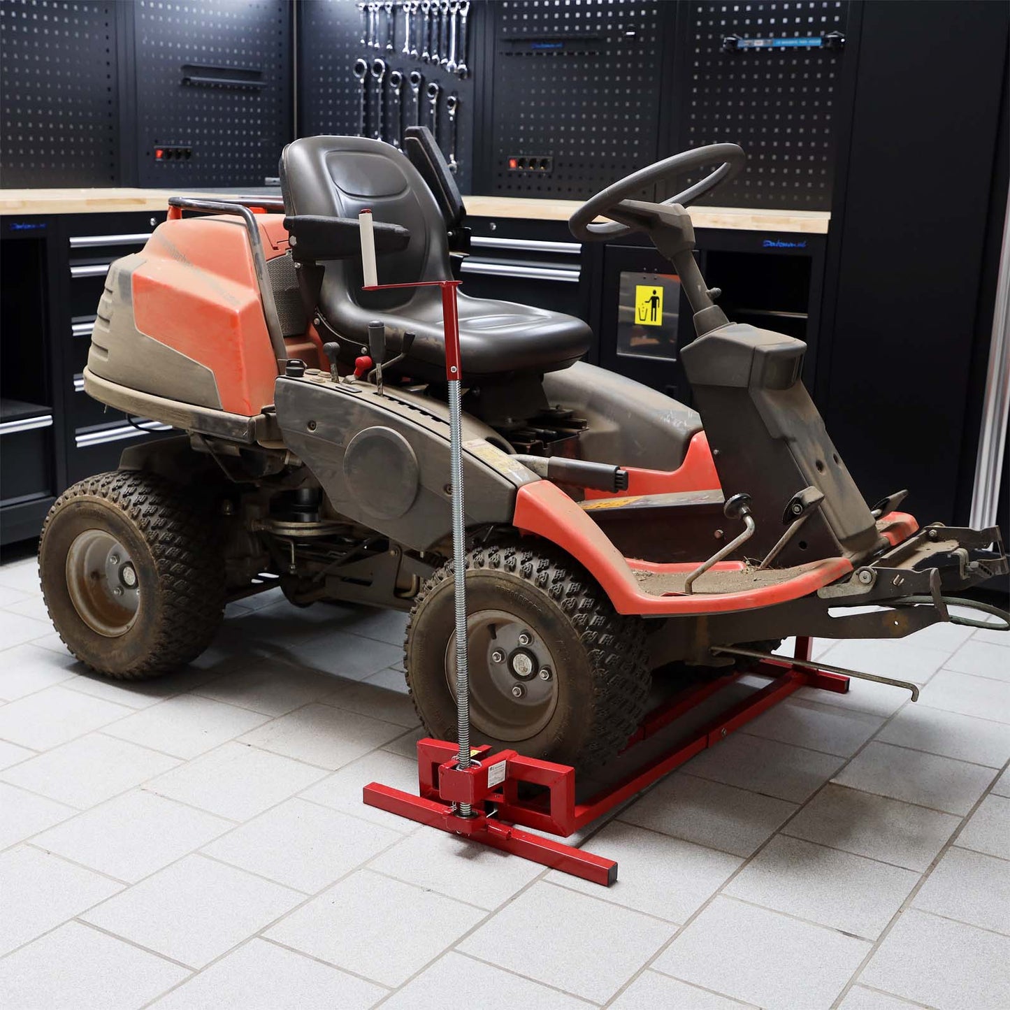 Red riding mower jack supporting a garden tractor in a garage workshop setting for maintenance