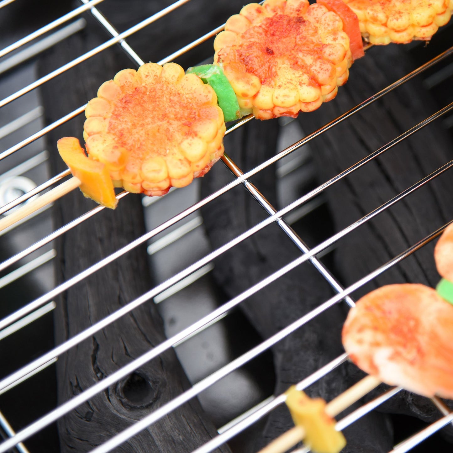 Sweet corn and bell pepper skewers with paprika grilling on a charcoal BBQ
