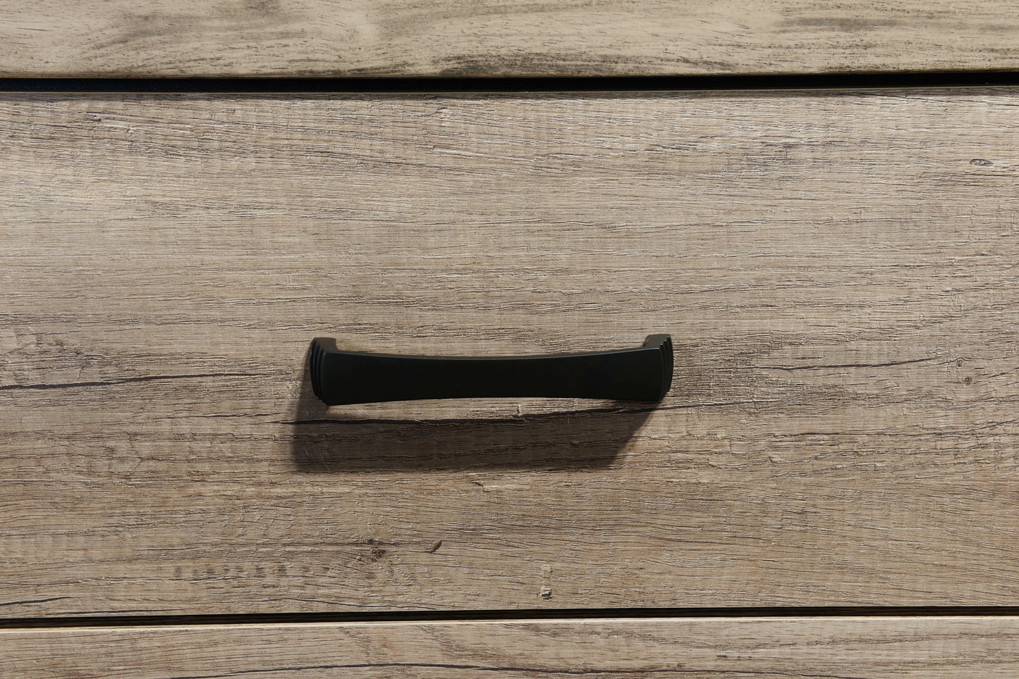 Black curved drawer pull on light wood grain dresser drawer