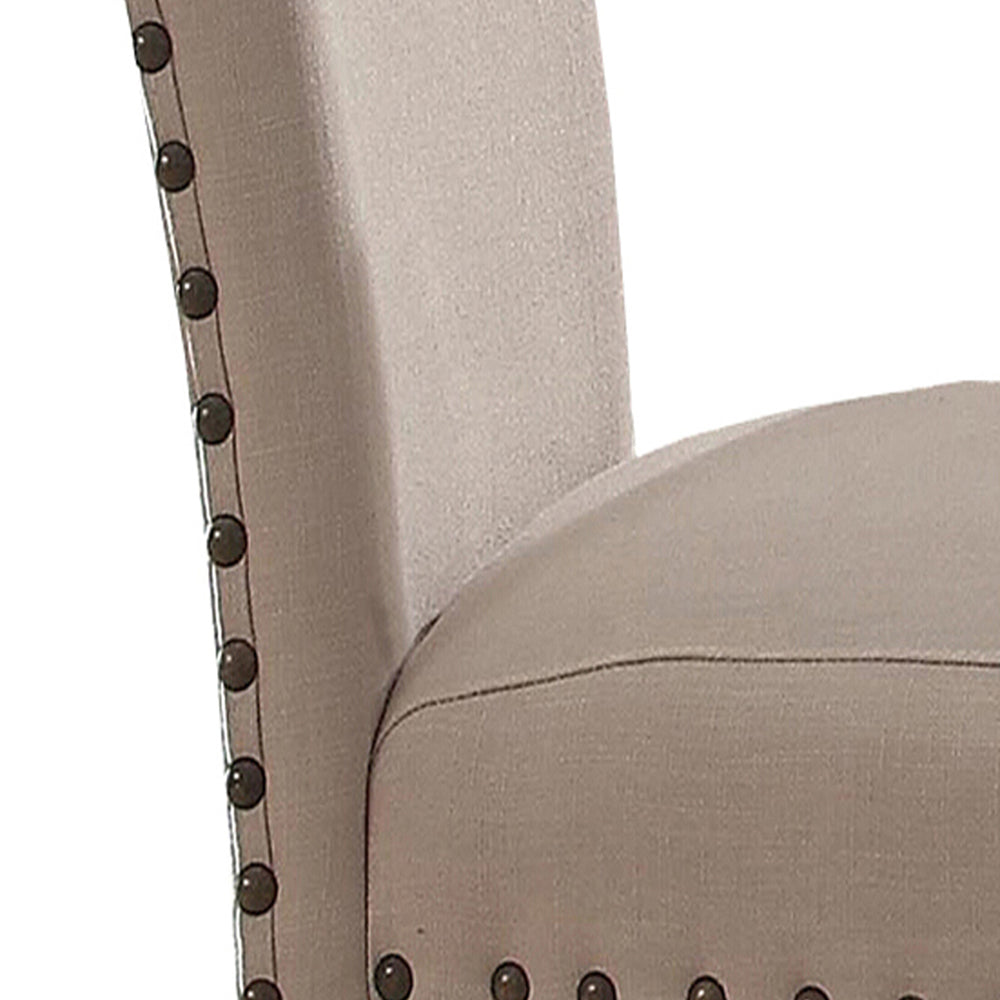Closeup of a beige linen wingback chair with decorative bronze nailhead trim on armrest